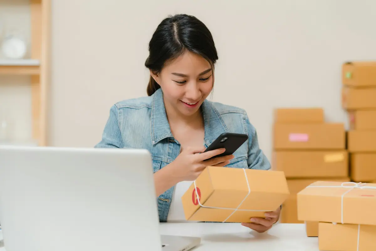 Vendedora revisando un pedido en el celular junto a sus paquetes listos para enviar